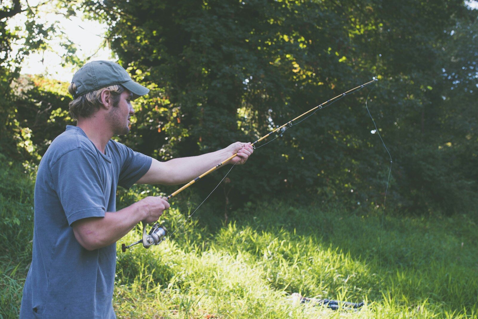 man in white t-shirt and black cap holding black fishing rod